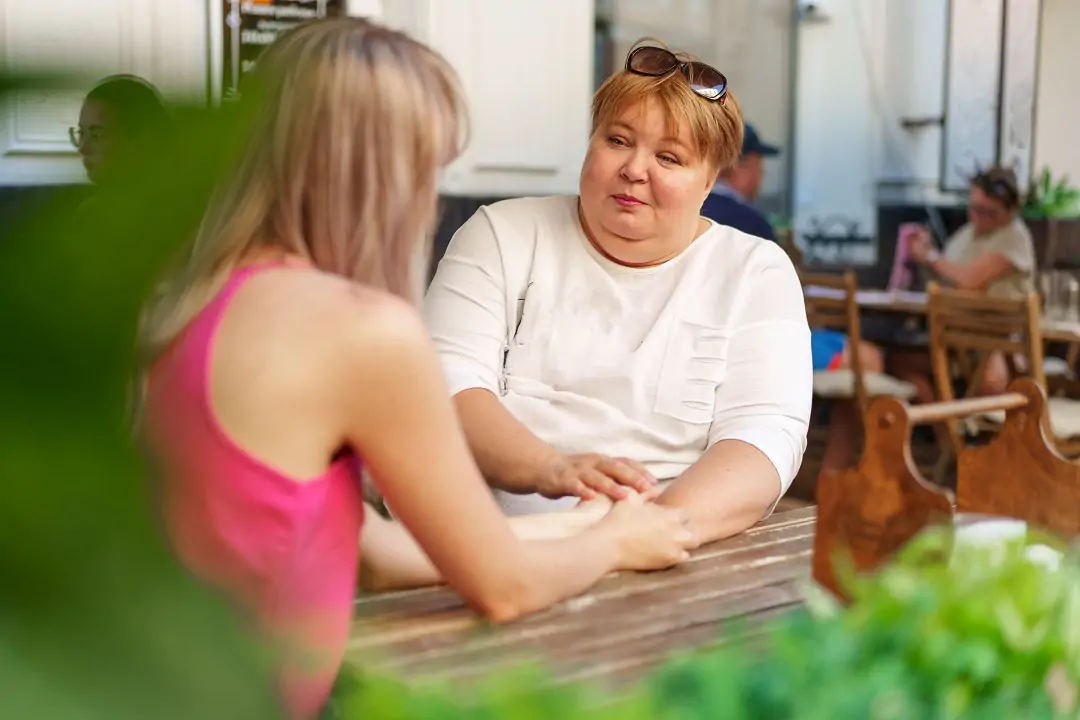 Mother with disability in wheelchair talking to her daughter while sitting at the table in cafe